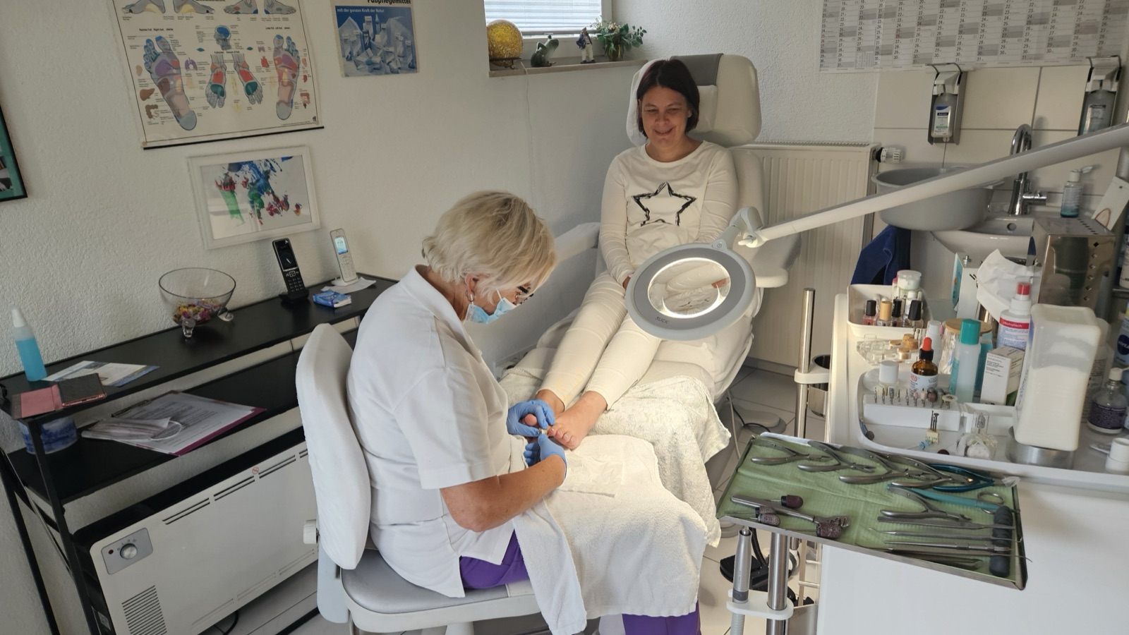 Angelika Murno-Fügel in der Fußpflegepraxis bei einer Behandlung, mit Mundschutz und Handschuhen